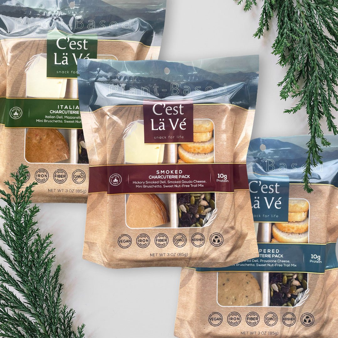 A photo of a C'est Lä Vé charcuterie Luncherie Snacks on gray background with green leaves on the edges